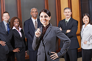 A Female Executive standing in front of a diverse group of other professionally dressed Executives standing in the background.